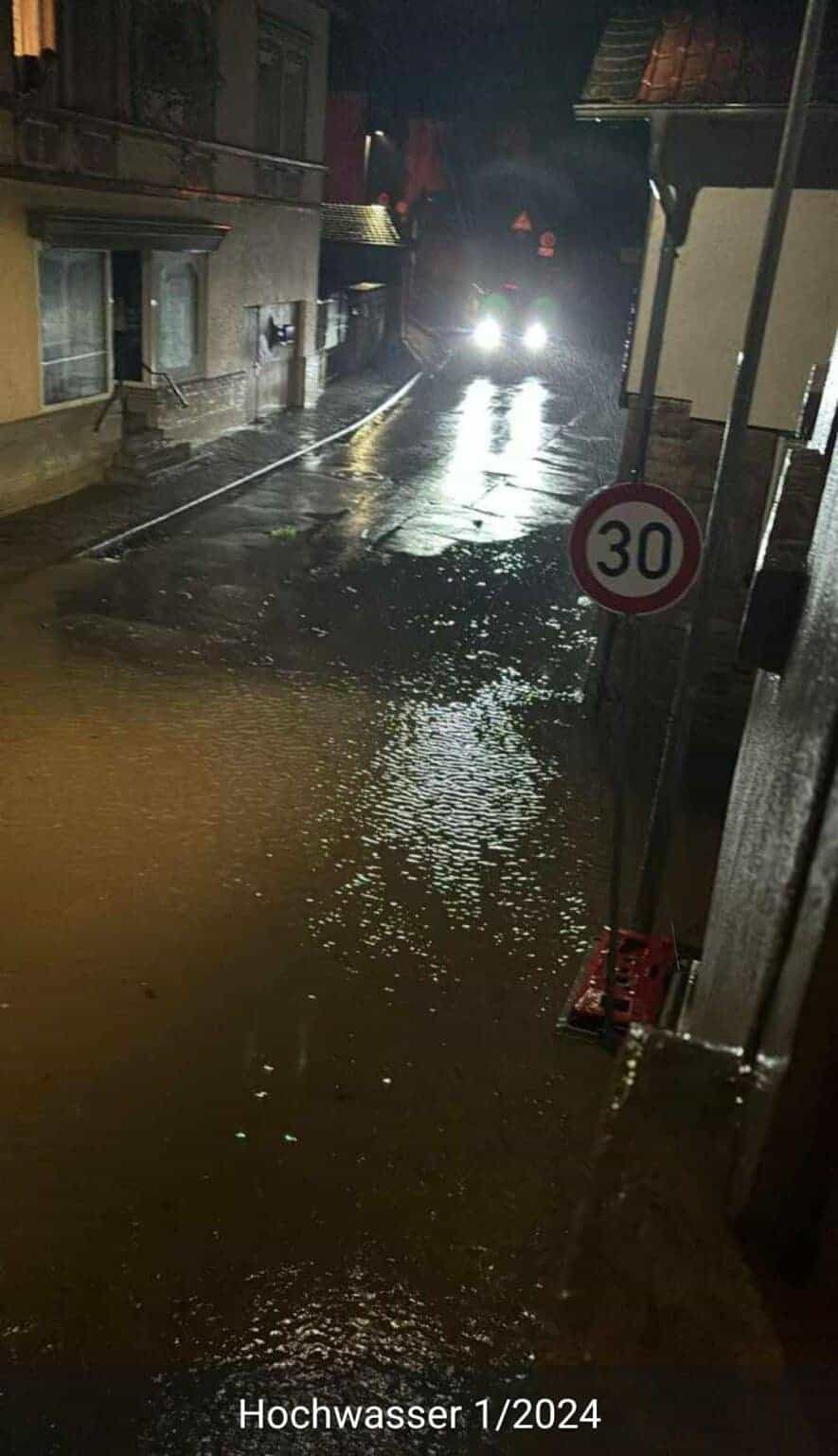 Eine stark überschwemmte Straße bei Nacht, auf der das Wasser bis zum Bordstein reicht.