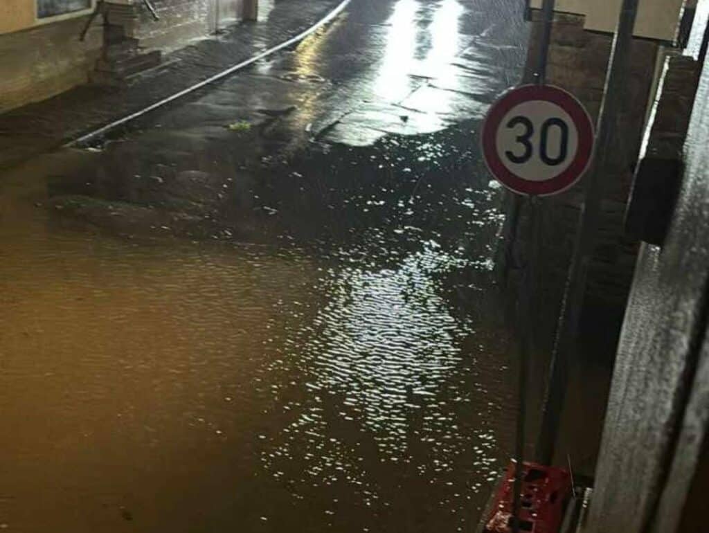 Eine stark überschwemmte Straße bei Nacht, auf der das Wasser bis zum Bordstein reicht.