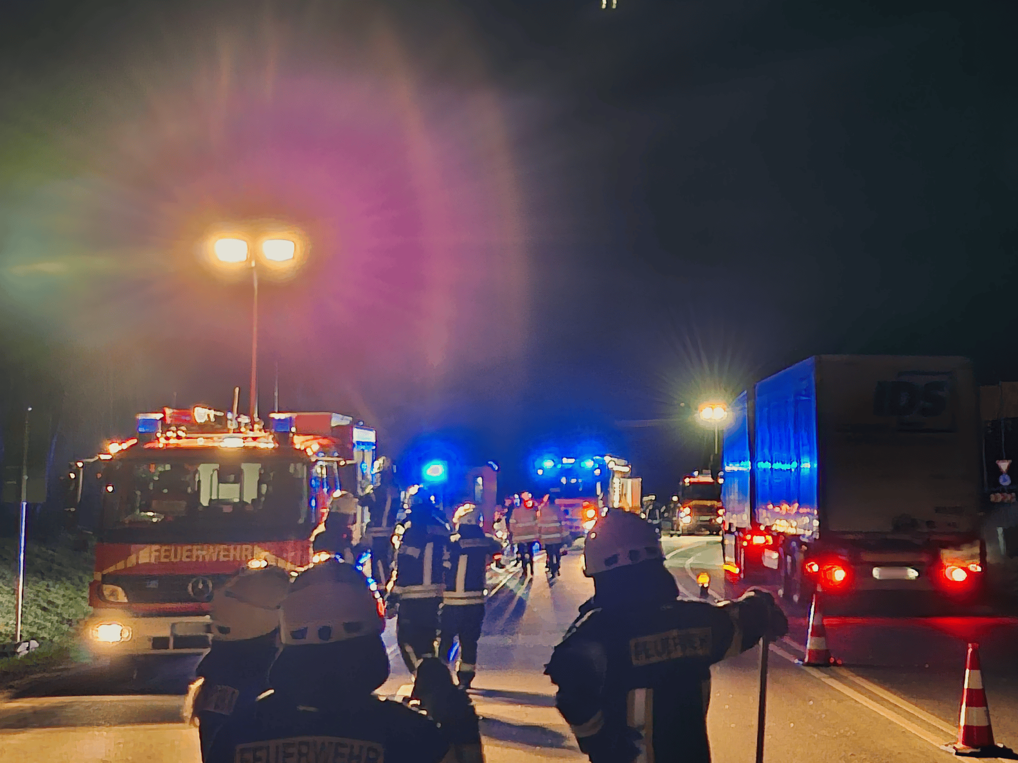 Einsatzfahrzeuge der Feuerwehr und Einsatzkräfte sichern eine Unfallstelle bei Nacht unter Beleuchtung.