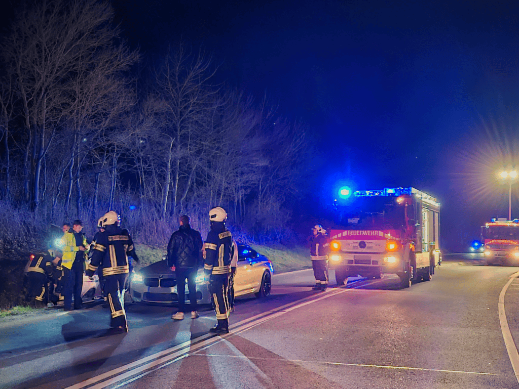 euerwehrkräfte und Polizei begutachten ein Fahrzeug im Straßengraben neben der Unfallstelle.