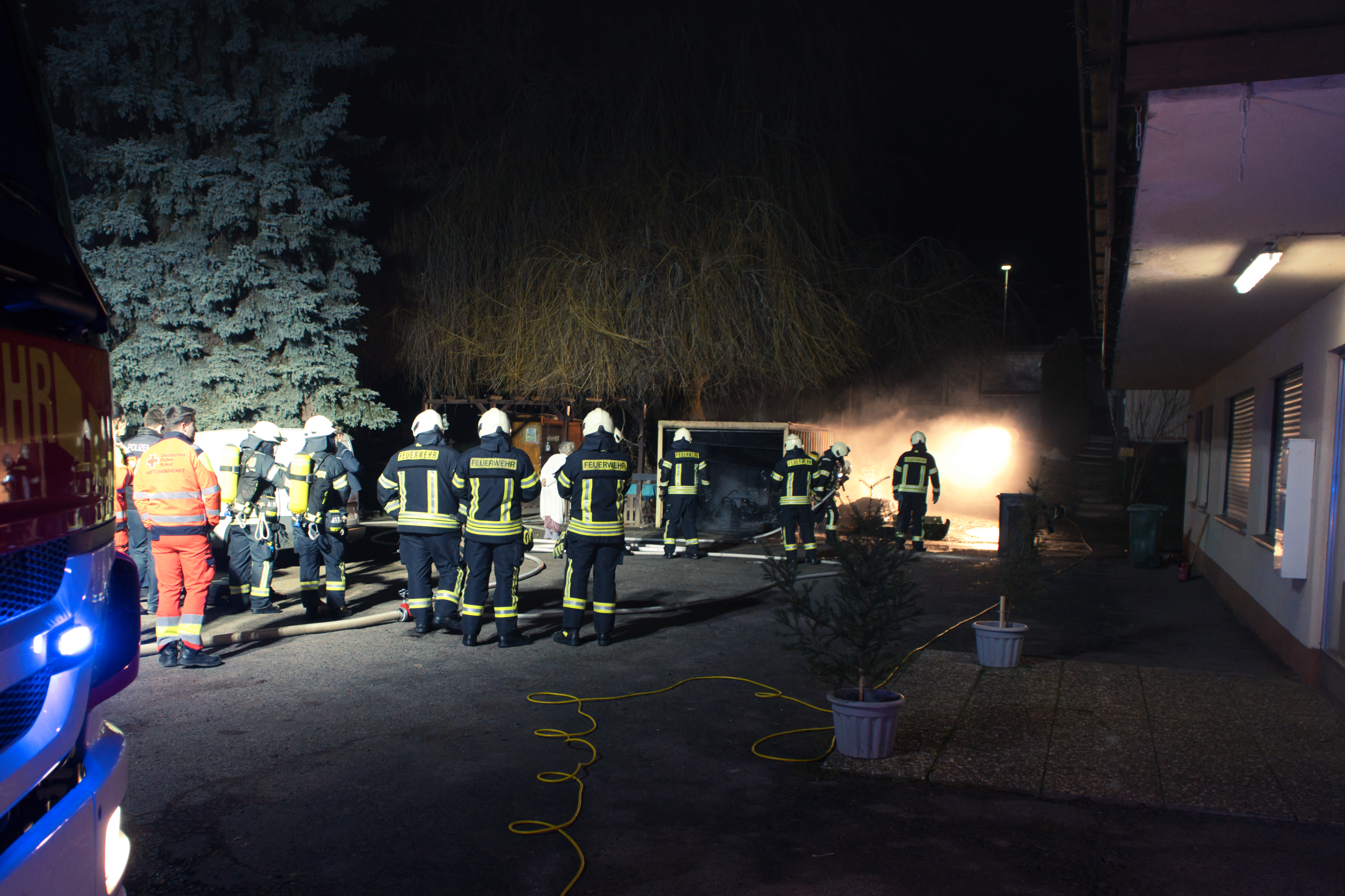 Feuerwehrkräfte im Einsatz bei einem nächtlichen Garagenbrand, unterstützt von Rettungskräften.