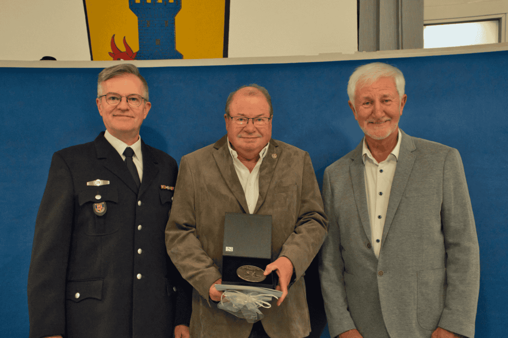 Karl-Wilhelm Haupt posiert mit der Medaille neben Wehrleiter Jürgen Mayer und Ortsvorsteher Uwe Frey.